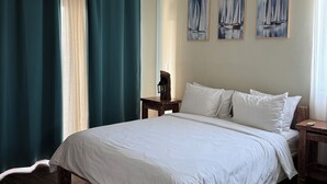 A bedroom with a bed, wooden headboard, a ceiling fan, a nightstand, a wall-mounted lamp, and sailboat paintings.
