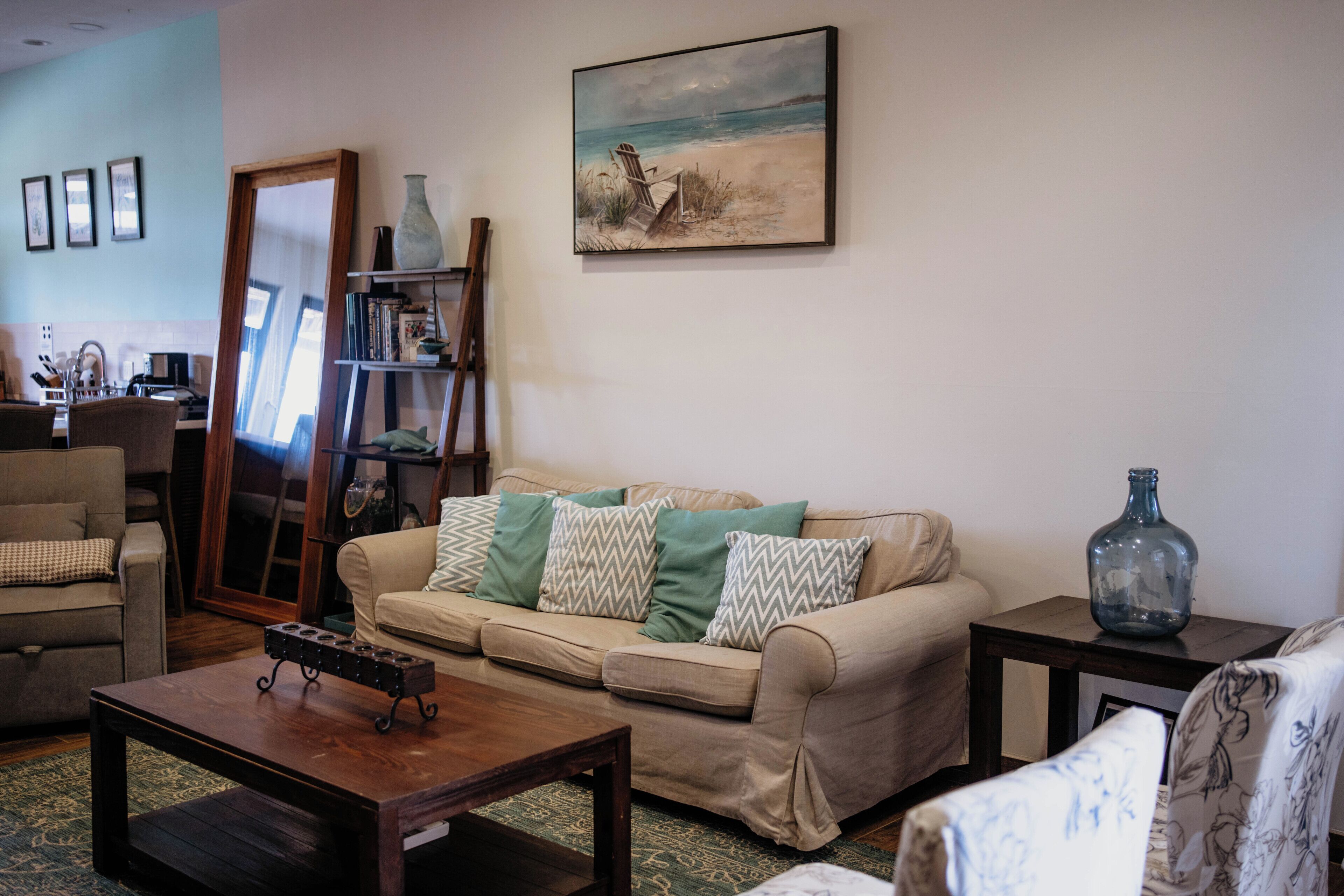 A living room with a beige sofa, a wooden coffee table, and a painting of a beach scene.