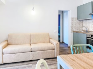 A living room with a sofa, a dining table, and a kitchen area with cabinets and a sink. - Oblo e Ginepro sul mare by Interhome (Cecina)