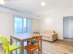 Huoneessa on ruokapöytä ja tuoleja, sohva sekä ovi, joka johtaa toiseen huoneeseen.
