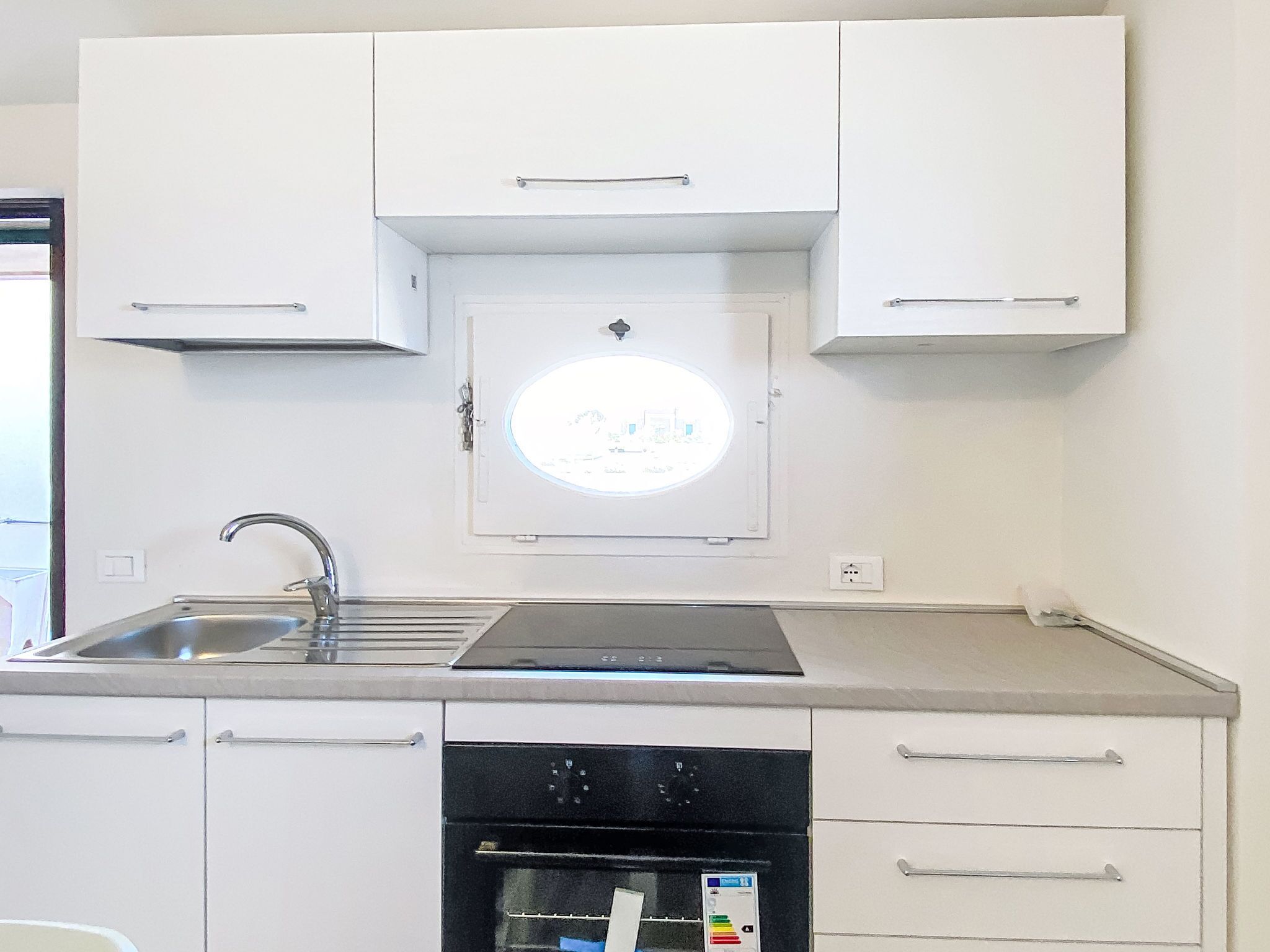 A kitchen with white cabinets, a stainless steel sink, a black dishwasher, and a built-in oven.
