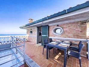 A terrace with a table set for dining, a brick wall, and a view of the sea. - Oblo e Ginepro sul mare by Interhome (Cecina)