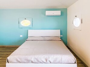 A single bed with a white headboard in a room with teal walls, a mounted air conditioner, and a circular window. - Oblo sul mare by Interhome (Cecina)