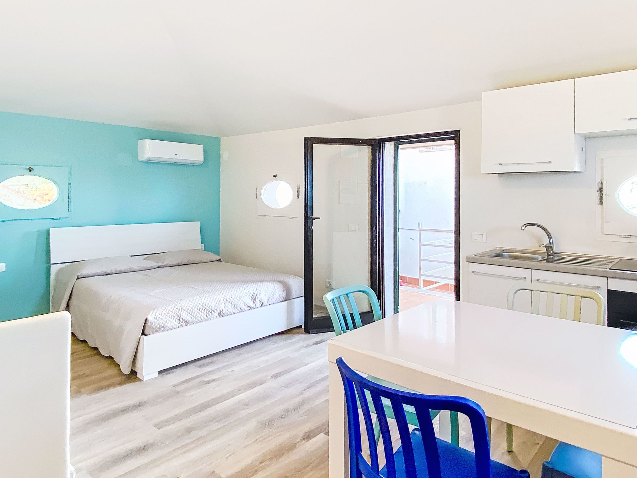 A bedroom with a bed, a chair, a small table, and a kitchenette.