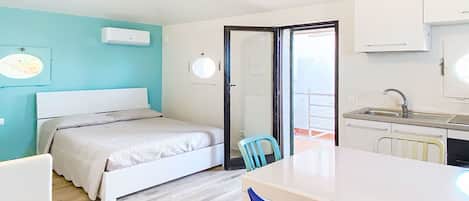 Un dormitorio con una cama, una silla, una mesita y un rincón de cocina.