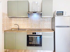 A compact kitchen with a sink, stove, oven, microwave, and cabinets. - Ginepro sul mare by Interhome (Cecina)
