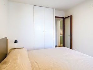 A bedroom with a bed, a wardrobe, a lamp, and a door leading to another room. - Ginepro sul mare by Interhome (Cecina)