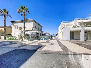 A coastal street with modern buildings, outdoor seating, and palm trees. - Ginepro sul mare by Interhome (Cecina)