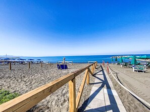 A wooden boardwalk leading to a beach with umbrellas and lounge chairs. - Ginepro sul mare by Interhome (Cecina)