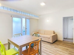 Een kamer met een eettafel, stoelen, een bank en een schuifdeur naar een buitenruimte.