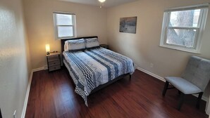 A bedroom with a bed, a nightstand, a chair, a ceiling fan, and two windows. - Remodeled Rossford Lower Apartment (Rossford)