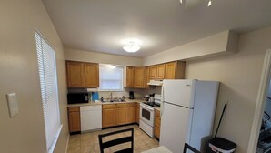 A kitchen with wooden cabinets, a white refrigerator, a stove, a sink, and a dining table with chairs. - Remodeled Rossford Lower Apartment (Rossford)
