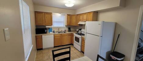 A kitchen with wooden cabinets, a white refrigerator, a stove, a sink, and a dining table with chairs.