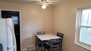 A kitchen with a white refrigerator, a dining table with four chairs, a ceiling fan, and a window. - Remodeled Rossford Lower Apartment (Rossford)