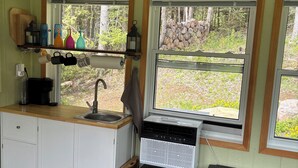 Une cuisine compacte équipée d’un évier, d’une cuisinière et d’un petit réfrigérateur. Elle comporte deux fenêtres donnant sur l’extérieur.