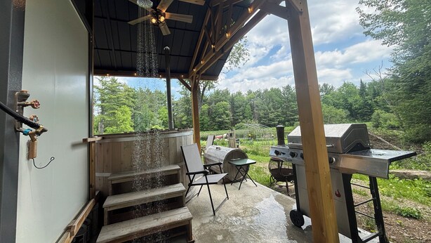 Un patio extérieur couvert, équipé d’un barbecue, d’un espace salon et d’un escalier menant à une terrasse.