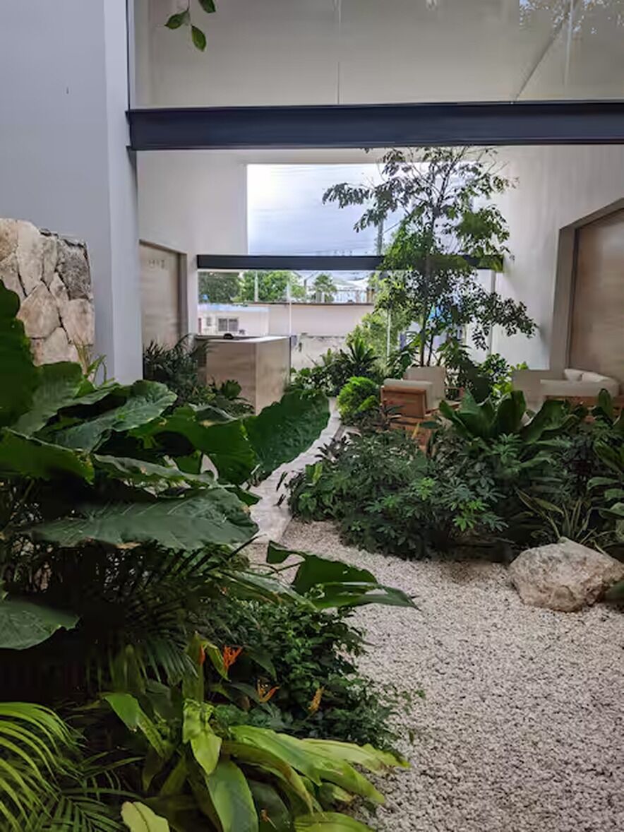 Een moderne binnentuin met verschillende planten, een zithoek en uitzicht op buiten.