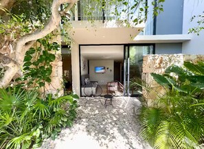 Un espace extérieur moderne, aménagé avec un mur en pierre, une porte vitrée donnant sur une pièce et une végétation luxuriante.