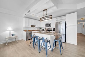 A modern kitchen with white cabinetry, stainless steel appliances, and a central island with bar stools. - Laketown Wharf 318 (Panama City Beach)