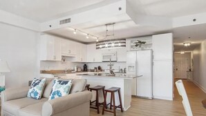 A modern kitchen with white cabinets, a central island, and a dining area with stools. - Laketown Wharf 318 (Panama City Beach)
