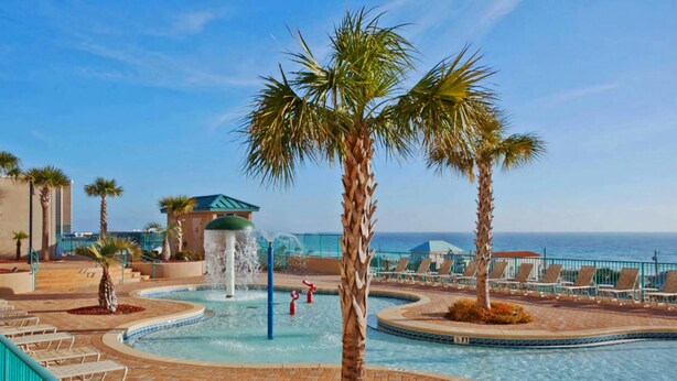 A pool area with palm trees, lounge chairs, and a water fountain. - Laketown Wharf 318 (Panama City Beach)
