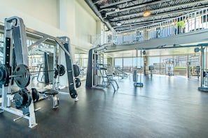 Ein geräumiges Fitnessstudio mit verschiedenen Gewichtstrainingsgeräten, einer Zwischenebene und Blick ins Freie.