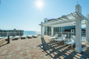 Eine sonnendurchflutete Terrassenanlage im Freien mit weißen Liegestühlen und einer Pergola, mit Blick auf das Meer.