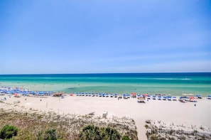Ein Strand mit vielen Sonnenschirmen und Liegestühlen, ein sandiger Uferstreifen und ein klarer, blauer Himmel.