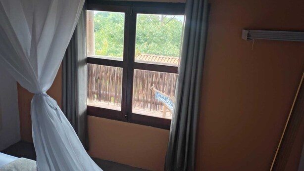 Une chambre avec un lit, une fenêtre avec des rideaux et une vue sur une terrasse en bois.