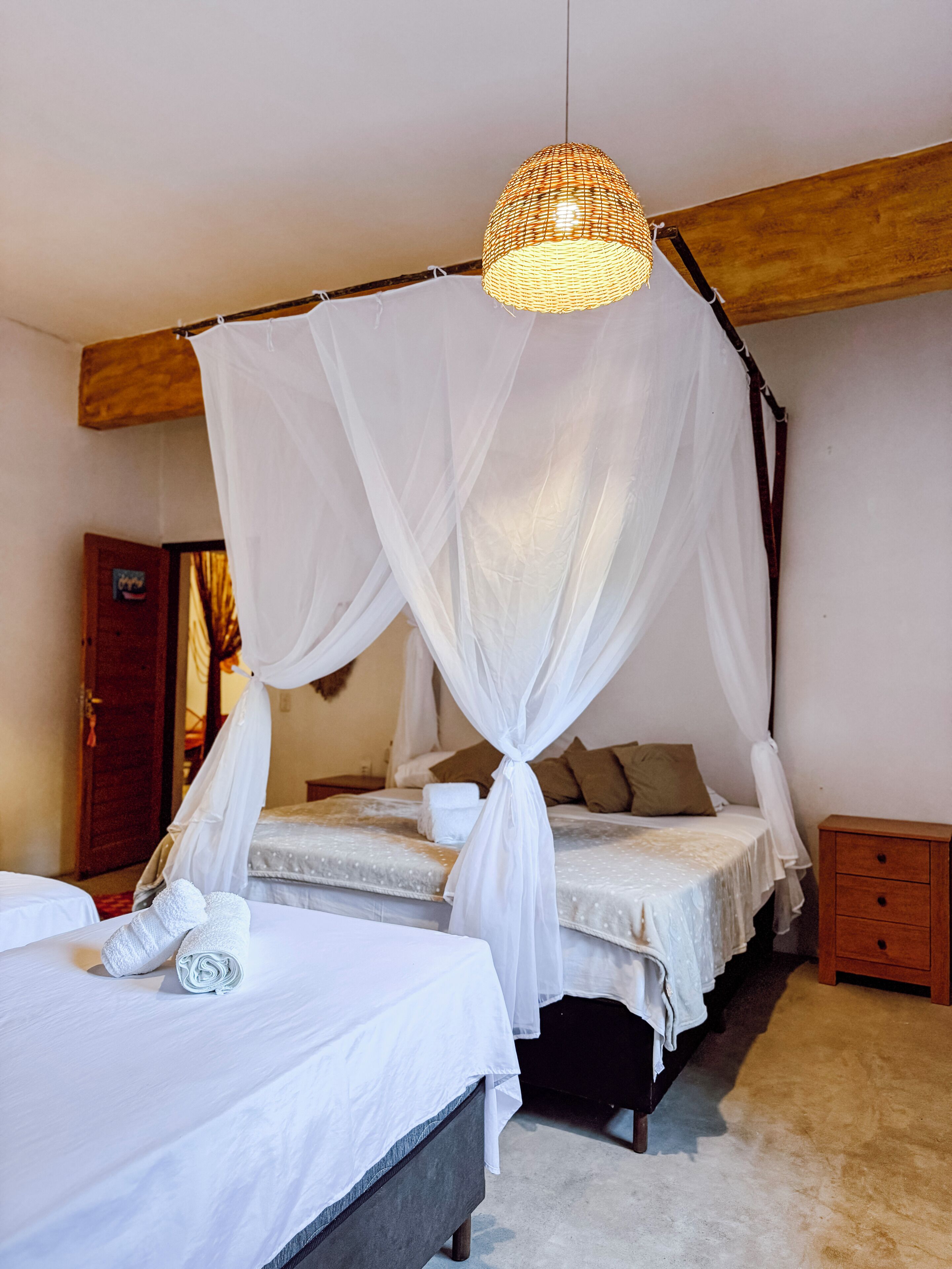 Quarto com duas camas, incluindo uma cama com dossel, cabeceira de madeira, mesa de cabeceira e luminária suspensa.