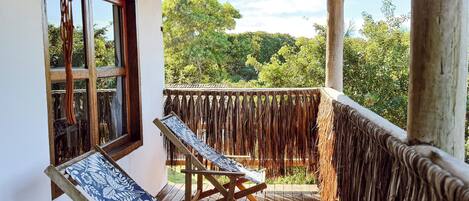Terraza de madera con dos sillones, una lámpara colgante y vistas a la vegetación.