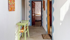 Un couloir avec une table verte, un luminaire suspendu et une porte donnant sur une chambre à coucher.