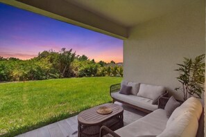 Eine Terrasse mit einer Couch, einem runden Tisch und Blick auf eine Wiese und Bäume.