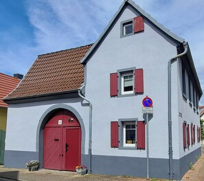 Ein zweistöckiges Gebäude mit roter Tür, mehreren Fenstern mit Fensterläden und einem Verbotsschild für Parken.