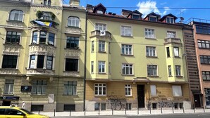 A yellow taxi on a city street, buildings with balconies, and a clear blue sky. - Spacious attic duplex in a heritage building in central Sarajevo (Sarajevo)