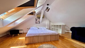 A modern loft bedroom with a sloped ceiling, a wooden bed, a round rug, and a built-in shelving unit. - Spacious attic duplex in a heritage building in central Sarajevo (Sarajevo)