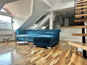 A modern loft with a blue sofa, a round white table, and a wooden staircase. - Spacious attic duplex in a heritage building in central Sarajevo (Sarajevo)