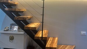 A modern staircase with wooden steps and metal railings, leading to a landing with a white cabinet and a framed picture. - Spacious attic duplex in a heritage building in central Sarajevo (Sarajevo)