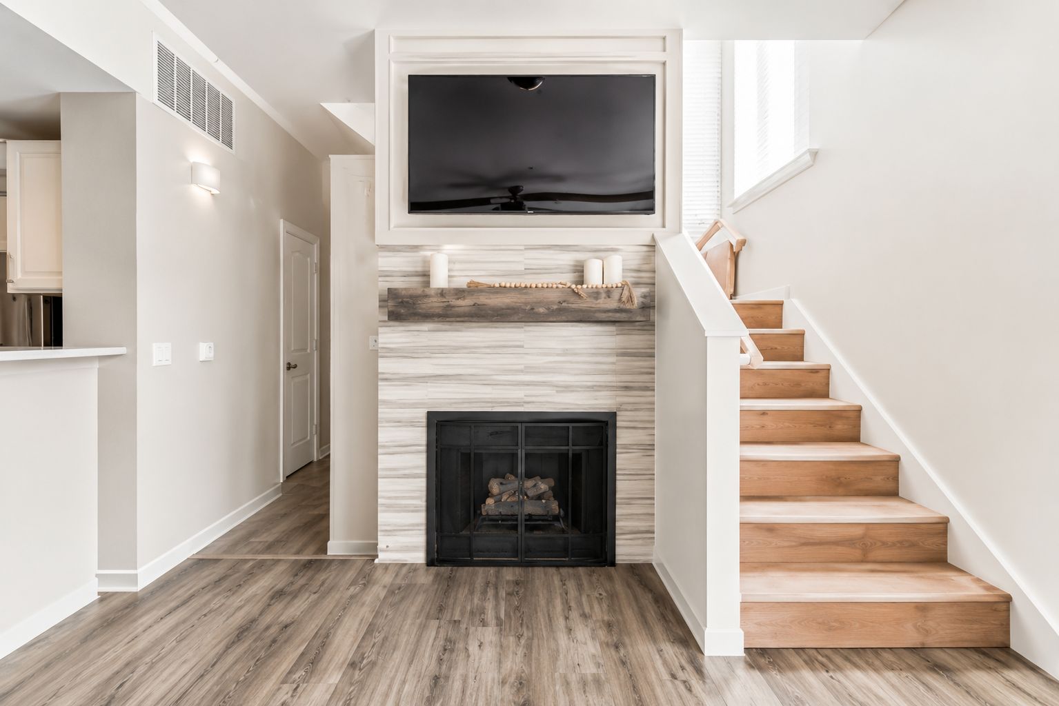 A staircase leading to a landing with a fireplace, a flat-screen TV mounted above it, and a hallway with wooden flooring.