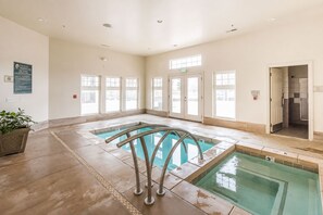 An indoor swimming pool with clear glass walls, a tiled floor, and a metal pool ladder. - Park City Mountain Views • Near Canyons Village • Hot Tub, Pool, Pets (Park City)