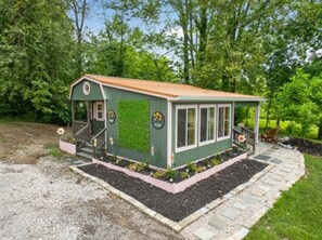 A small, single-story building with a sloped roof, a front porch, and a garden area with a pathway leading to the entrance. - 3 Tiny Cabins Together Lakefront (Indianapolis)