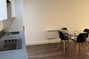 A modern kitchen with a built-in stove, a sink, and a dining area with a glass table and black chairs. - Central Broad St Apartment, Gym & Fast Wifi (Birmingham)