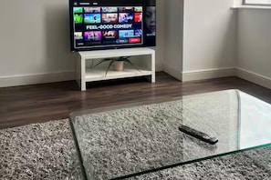 A television on a stand with a remote control on a glass table. - Central Broad St Apartment, Gym & Fast Wifi (Birmingham)