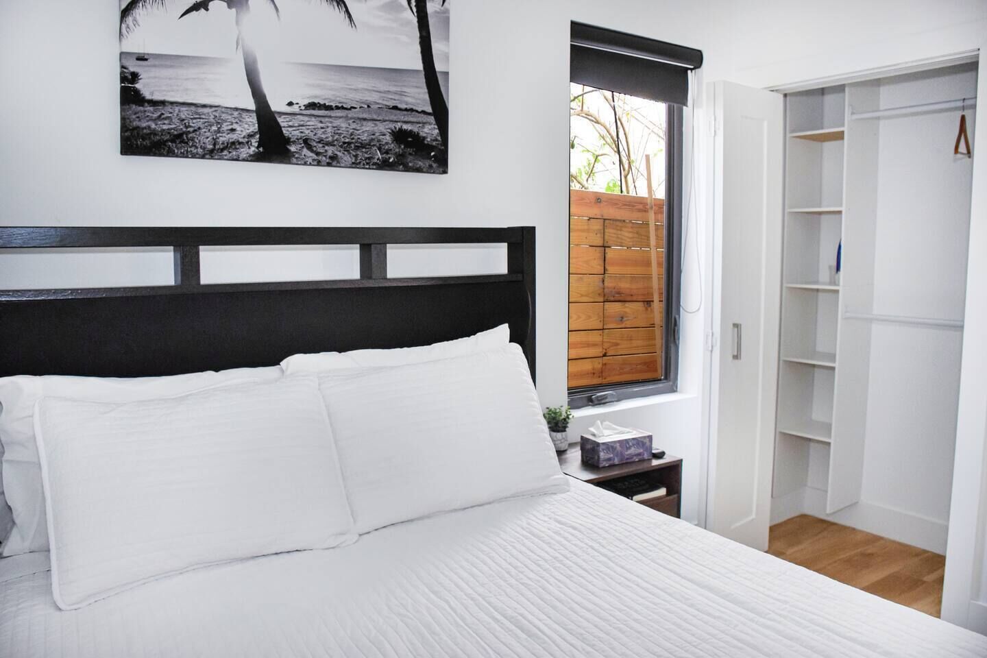 A bedroom with a bed, a nightstand, a window with a view of the outside, and a wardrobe.