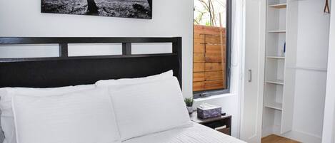 A bedroom with a bed, a nightstand, a window with a view of the outside, and a wardrobe.