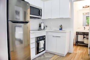Cocina compacta con armarios blancos, un refrigerador de acero inoxidable, un microondas, un horno y un lavamanos.