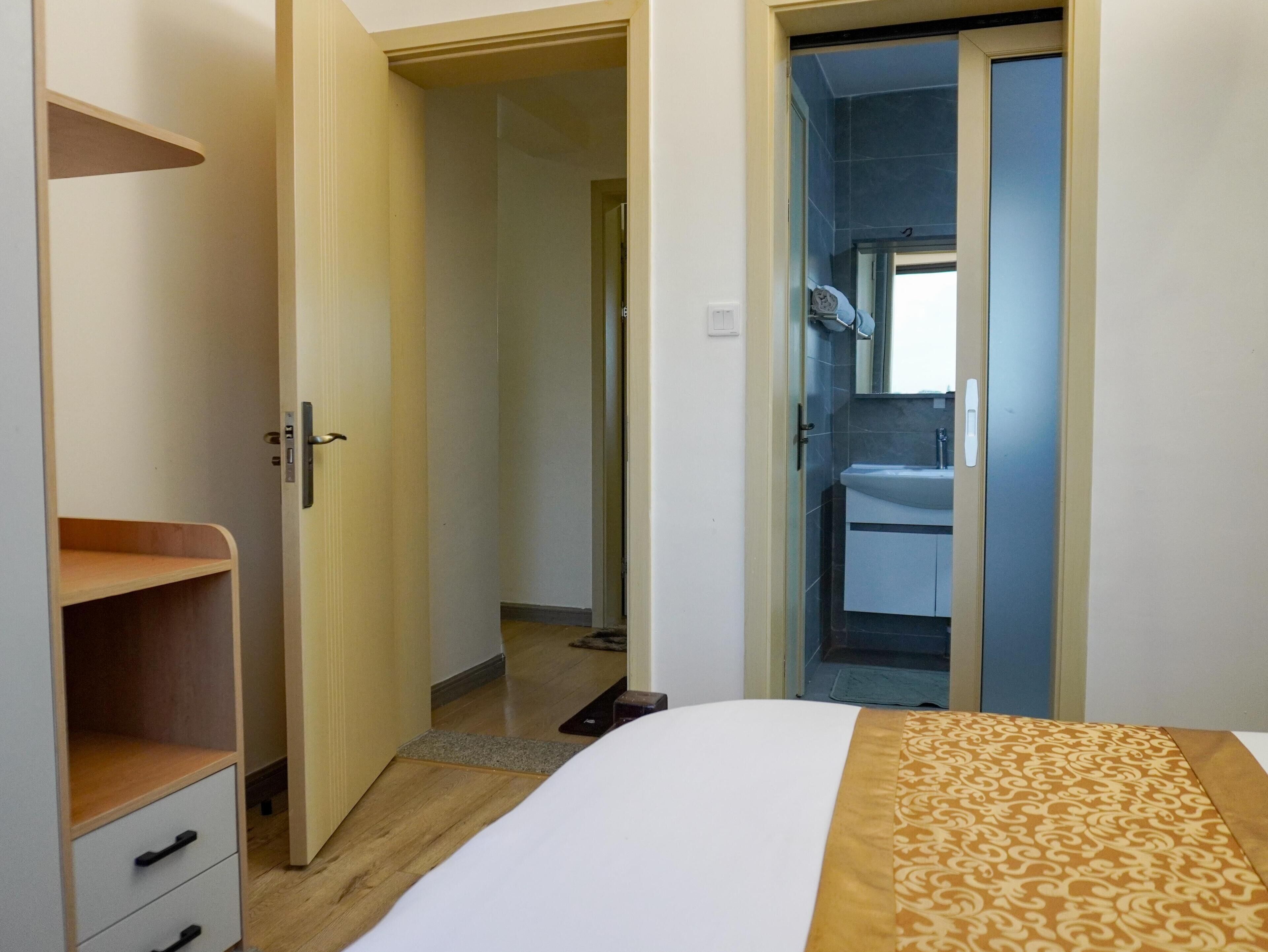 Une chambre d’hôtel comprenant un lit, une armoire, une salle de bain avec un lavabo et un miroir, et une porte donnant sur une autre pièce.