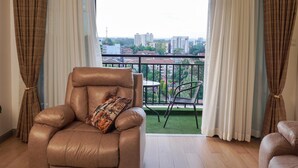 Ein Wohnzimmer mit einer Ledersofa, einem gemusterten Zierkissen, einem Esstisch mit Stühlen und Blick auf eine Stadtlandschaft durch große Fenster.