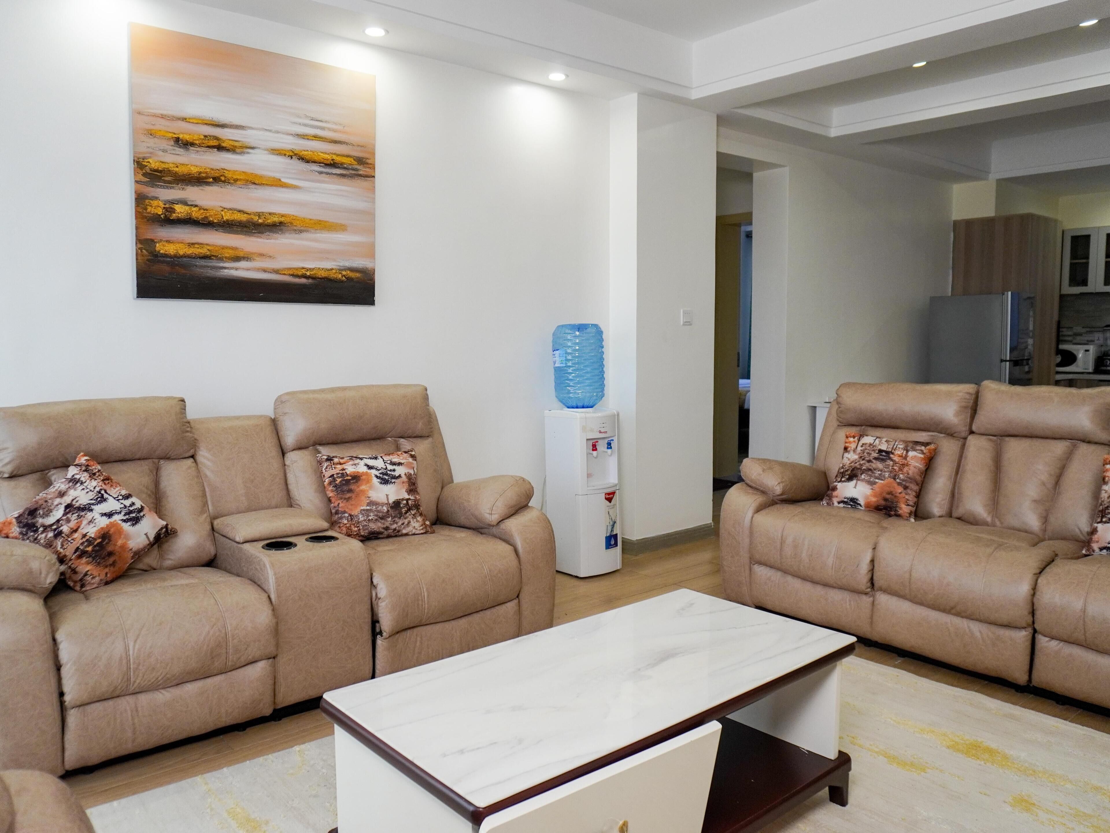 A modern living room with two beige sofas, a marble coffee table, and a water dispenser.