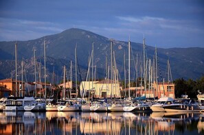 Marina com vários veleiros atracados, montanha ao fundo e edifícios com telhados vermelhos.